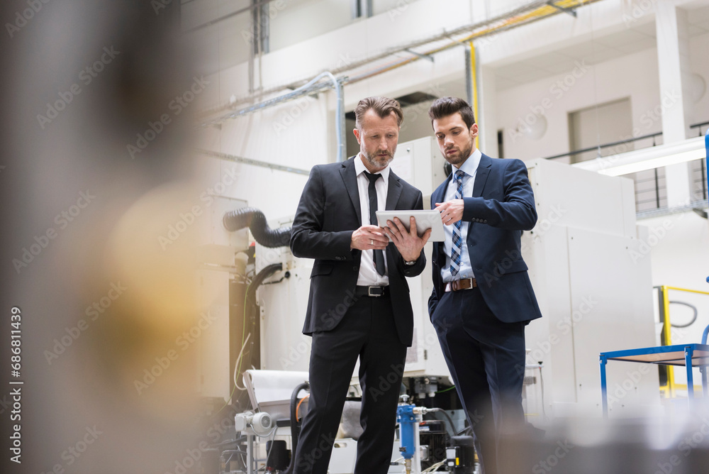 Two businessmen sharing tablet in factory shop floor