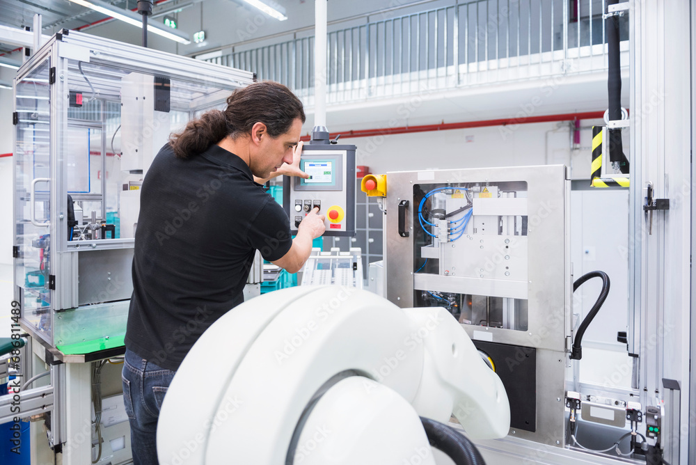 Man operating assembly robot in factory Man operating assembly robot in factory