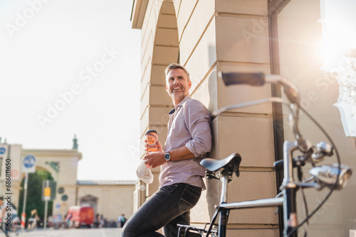 Smiling man with bicycle and takeaway coffee in the city