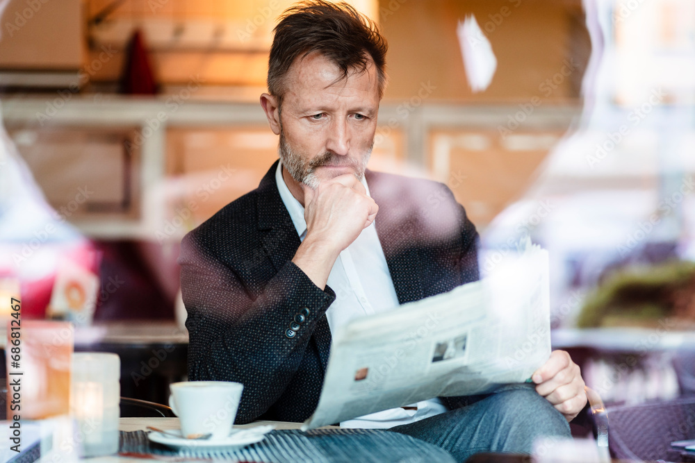 Portrait of pensive mature businessman reading newspaper in a coffee shop
