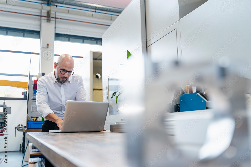 Focused businessman using laptop in factory Focused businessman using laptop in factory