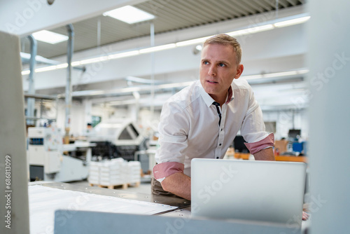 Businessman with laptop in a factory looking around