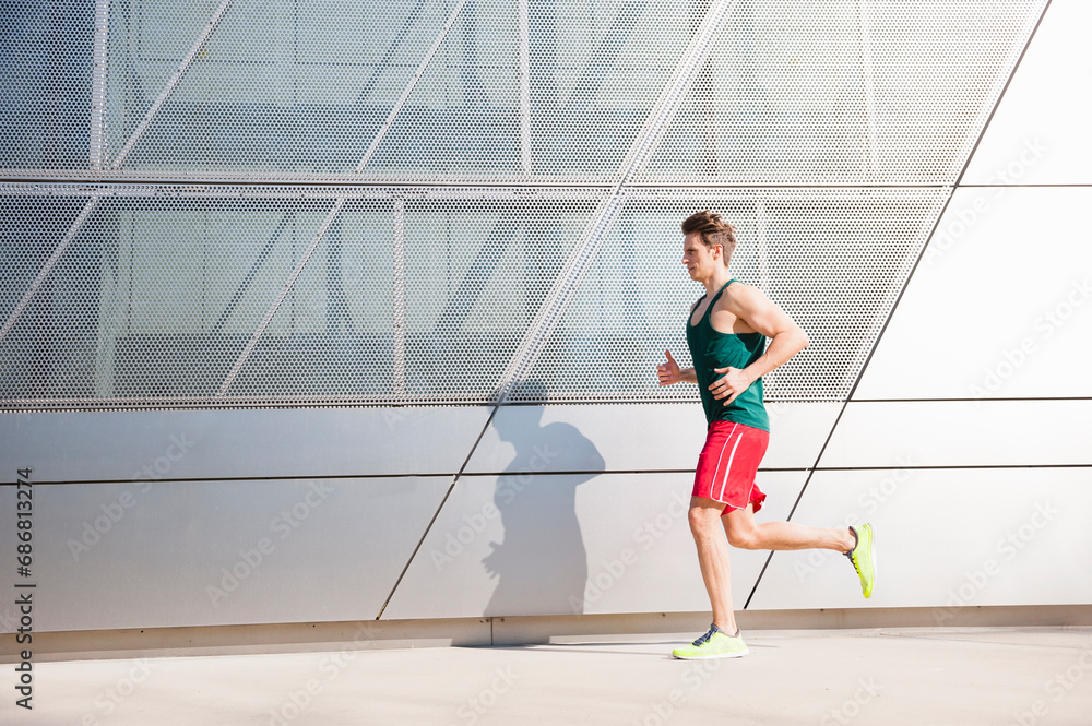 Mid adult man running on sidewalk by modern building in city Mid adult man running on sidewalk by modern building in city