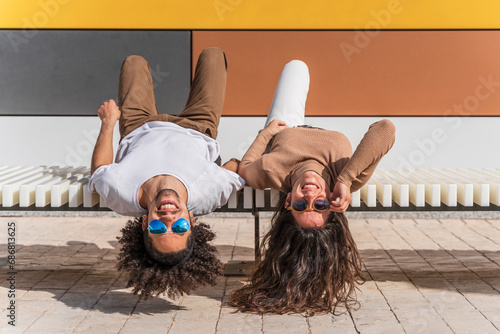 Couple with sunglasses, relaxing on bench, lying on back, heads hanging down photo