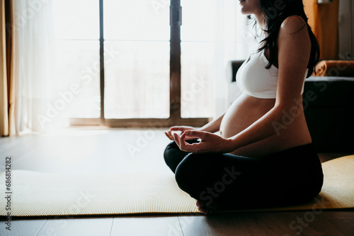 Pregnant woman meditating while sitting on exercise mat at home photo