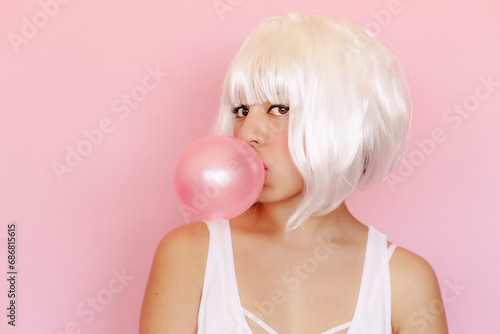 Portrait of young woman with pink gum bubble in front of pink background photo