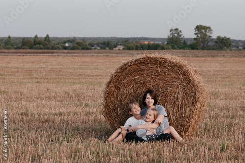Woman with two kids sitting near a haystack on a stubble field photo
