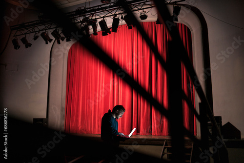 Director standing in front of stage at theatre using laptop
