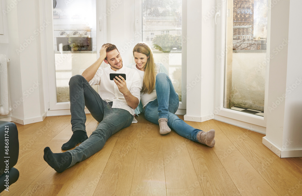 Smiling couple sitting on floor looking at cell phone