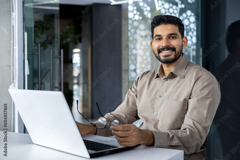 Portrait of accountant financier at workplace, businessman with laptop smiling and looking at camera inside office at workplace, man in shirt happy with achievement results and successful reports. Portrait of accountant financier at workplace, businessman with laptop smiling and looking at camera inside office at workplace, man in shirt happy with achievement results and successful reports.