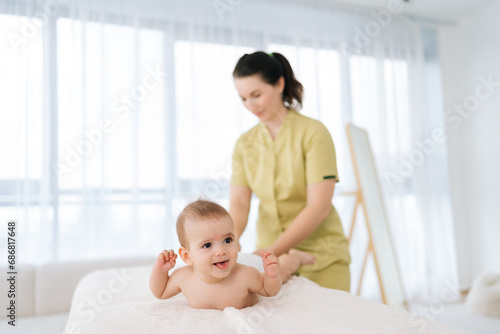 Selective focus of happy smiling infant boy having legs massage. Female doctor doing gymnastics and foot massage to toddler baby. Nurse in uniform doing orthopedic leg exercises to cute child.