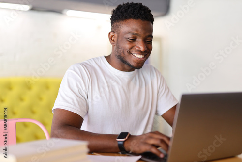 Happy young businessman using a laptop at a modern home office, exuding confidence and professionalism.