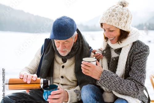 Behang Senior couple having a break with hot beverages in snow-covered winter landscape