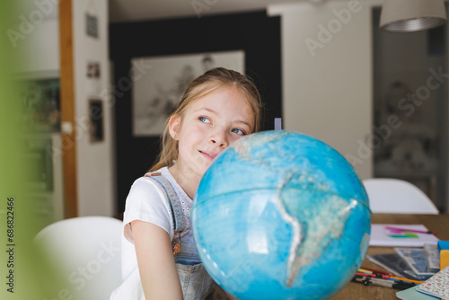 Portrait of confident girl with globe at home looking at distance