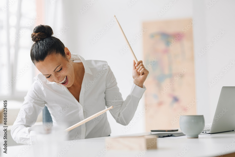 Cheerful female entrepreneur playing drumsticks on desk while screaming in home office Cheerful female entrepreneur playing drumsticks on desk while screaming in home office