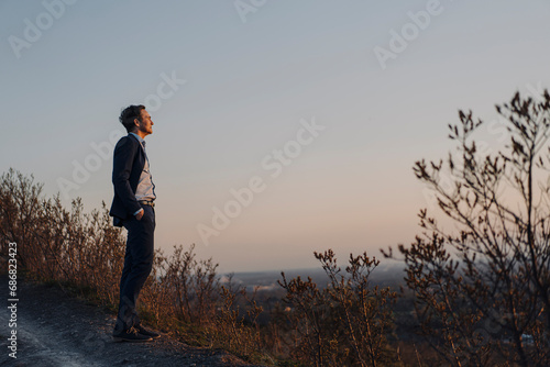Mature businessman standing on a disused mine tip at sunset looking at view