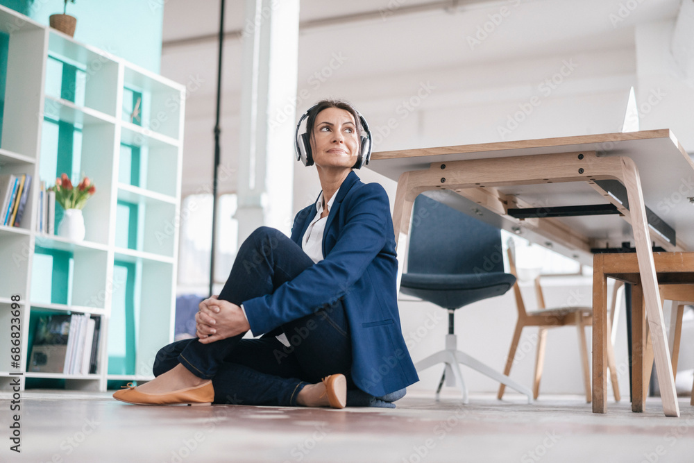 Businesswoman sitting on the floor in a loft listening music with headphones Businesswoman sitting on the floor in a loft listening music with headphones