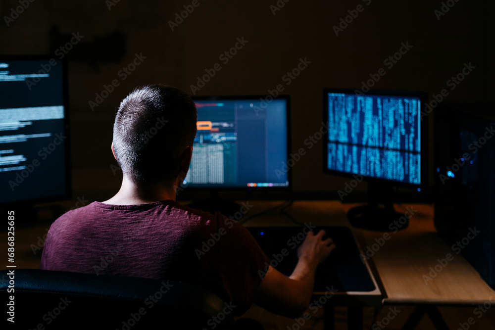 Hacker using computer while sitting in dark office Hacker using computer while sitting in dark office
