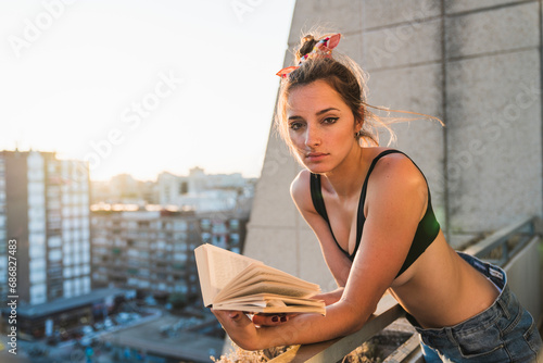 Portrait of young woman wearing bra reading book on balcony