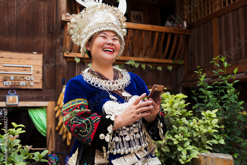 China, Guizhou, laughing Miao woman wearing traditional dress and headdress holding cell phone photo