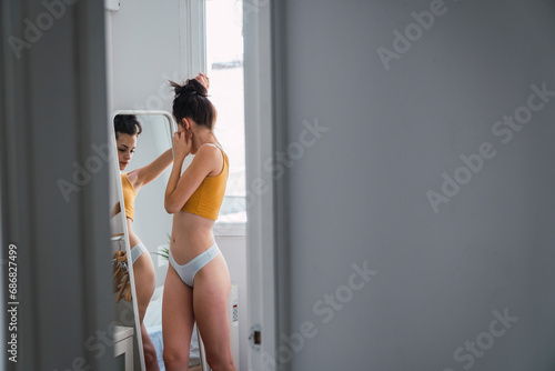 Young woman in underwear at home looking in mirror