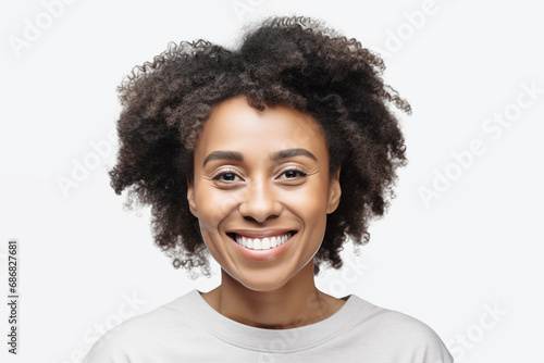 Studio portrait of a beautiful middle age woman with black curly hair. Laughing woman wearing white t-shirt looking at camera. Isolated on grey background. People, lifestyle, beauty concept
