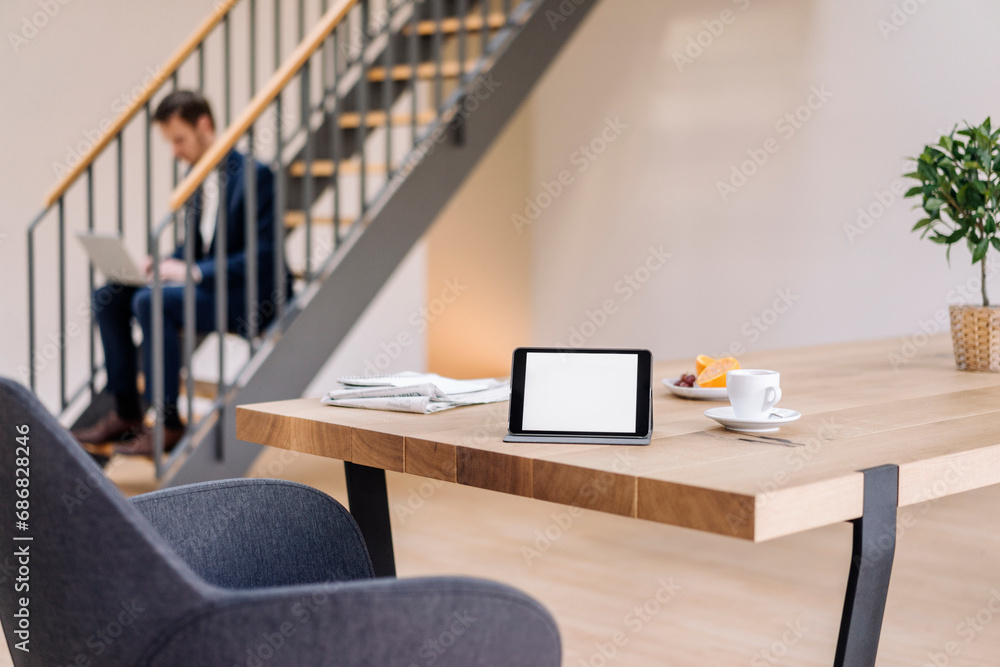 Tablet on table with businessman on stairs using laptop in background Tablet on table with businessman on stairs using laptop in background