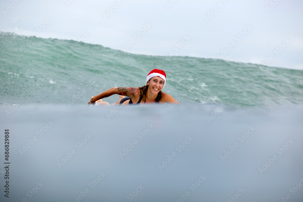 Indonesia, Bali, smiling woman on surfboard wearing Santa hat