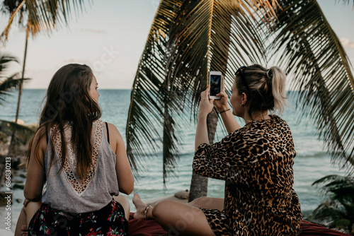 Mexico, Quintana Roo, Tulum, two young women with cell phone relaxing on the beach photo