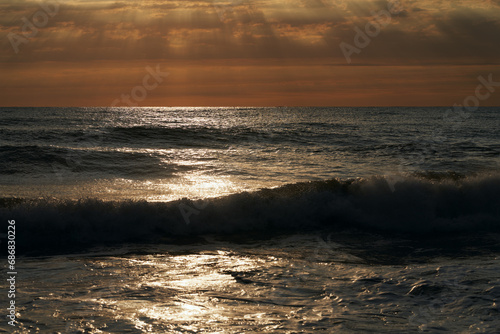 Panoramic view of the sea surface at sunset. Surf waves glisten in the sunlight. Picturesque natural background. Copy space.
