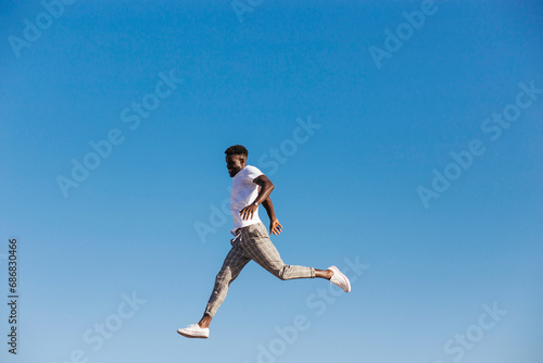 Young man jumping against clear blue sky during sunny day