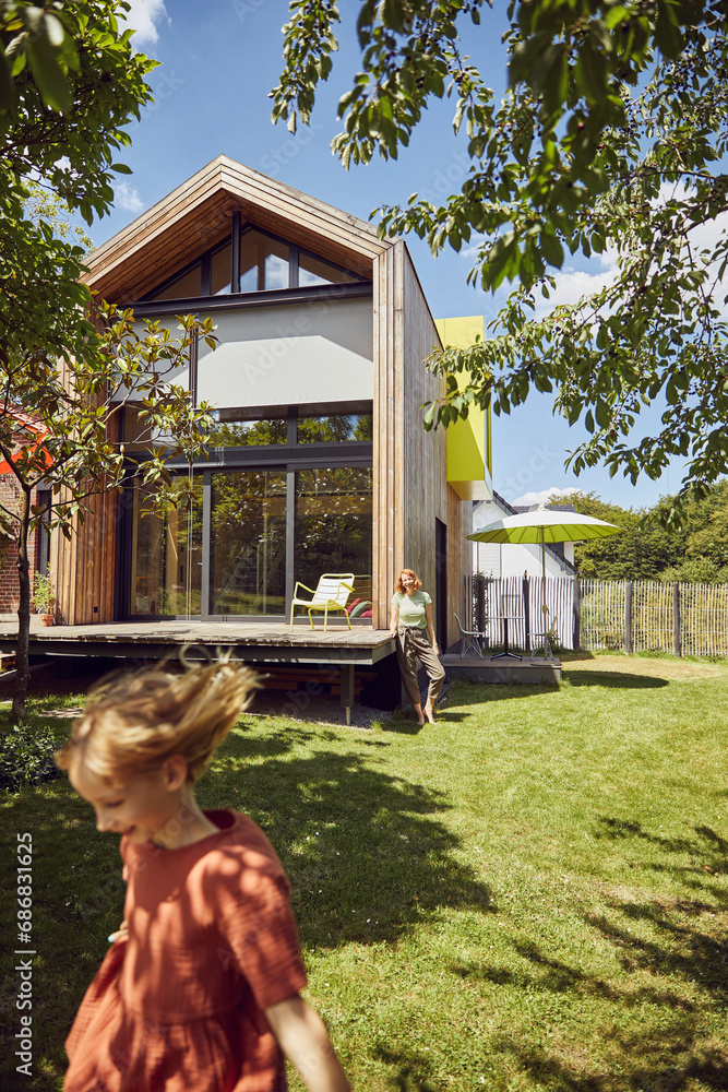 Mother with daughter standing on grassy land in yard outside tiny house