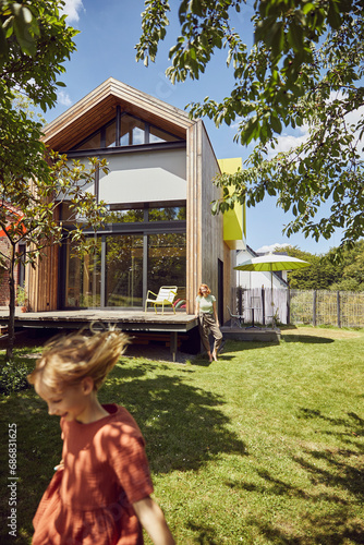 Obraz na płótnie Mother with daughter standing on grassy land in yard outside tiny house w salonie