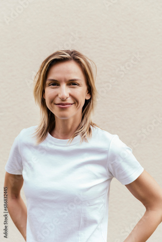 Portrait of smiling blond woman wearing white t-shirt in front of light wall