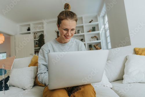 Smiling woman working on laptop while sitting on sofa at home