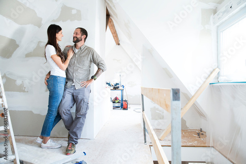 Smiling couple standing in attic to be renovated