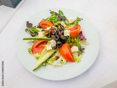 A Greek salad with cucumbers, tomatoes, olives and feta cheese is on a plate in the restaurant