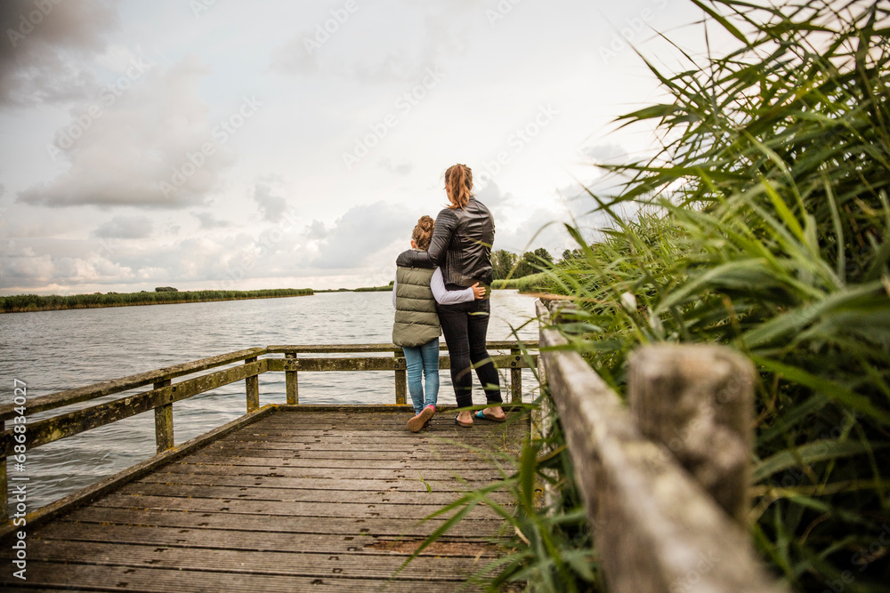 Mother and daughter standing on jetty at a lake
