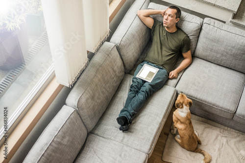 Man at home with tablet on the couch with dog beside him photo