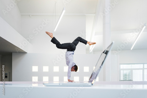 Businessman doing a handstand at laptop in office photo