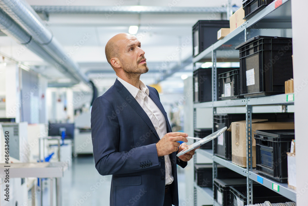 Mature male professional with digital tablet looking at containers on rack in industry Mature male professional with digital tablet looking at containers on rack in industry
