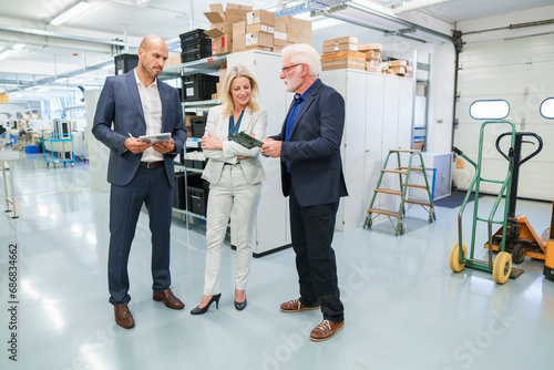 Senior businessman discussing over machine part with colleagues at illuminated industry