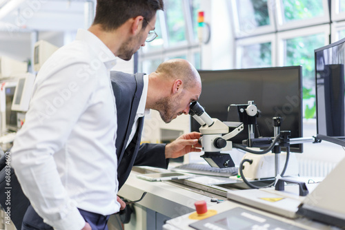 Young male technician standing by businessman looking through microscope at laboratory
