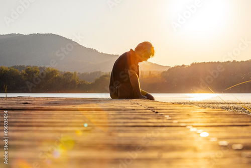 Senior man sitting on a wooden footbridge and looking down, against the sun photo
