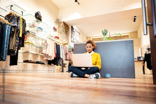 Young woman working in fashion store, using laptop