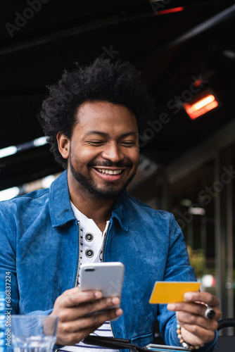 Smiling man using credit card and smart phone for paying at sidewalk cafe photo