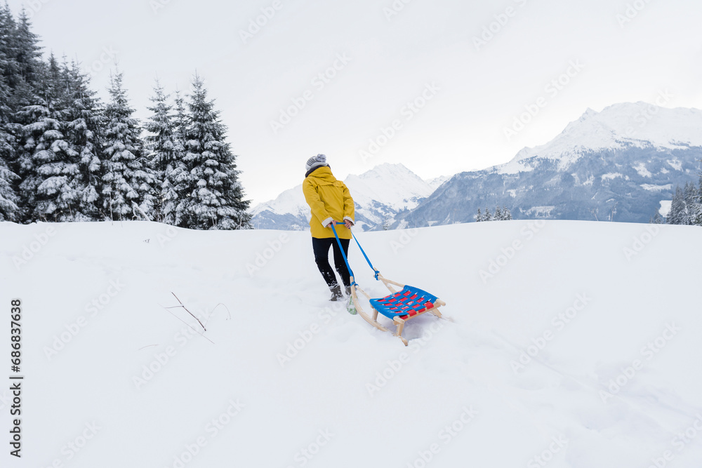 Austria, Tyrol, Thurn, back view of woman pulling sledge in snow-covered landscape