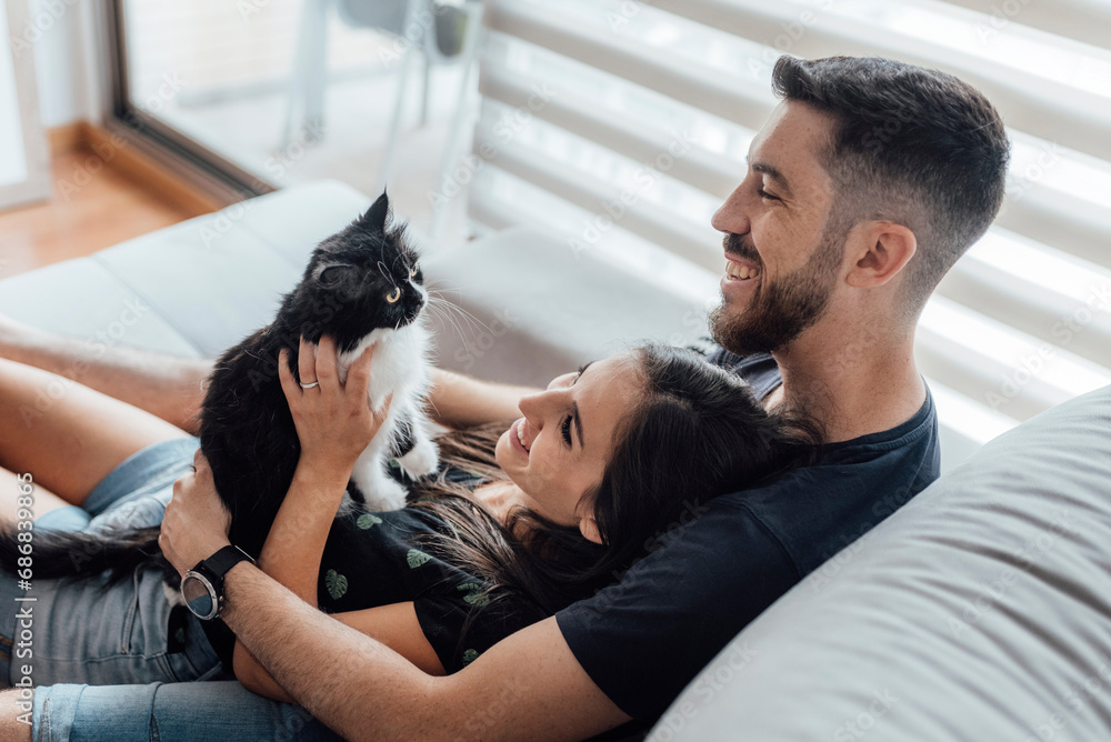 Happy couple spending leisure time with cat while sitting at home