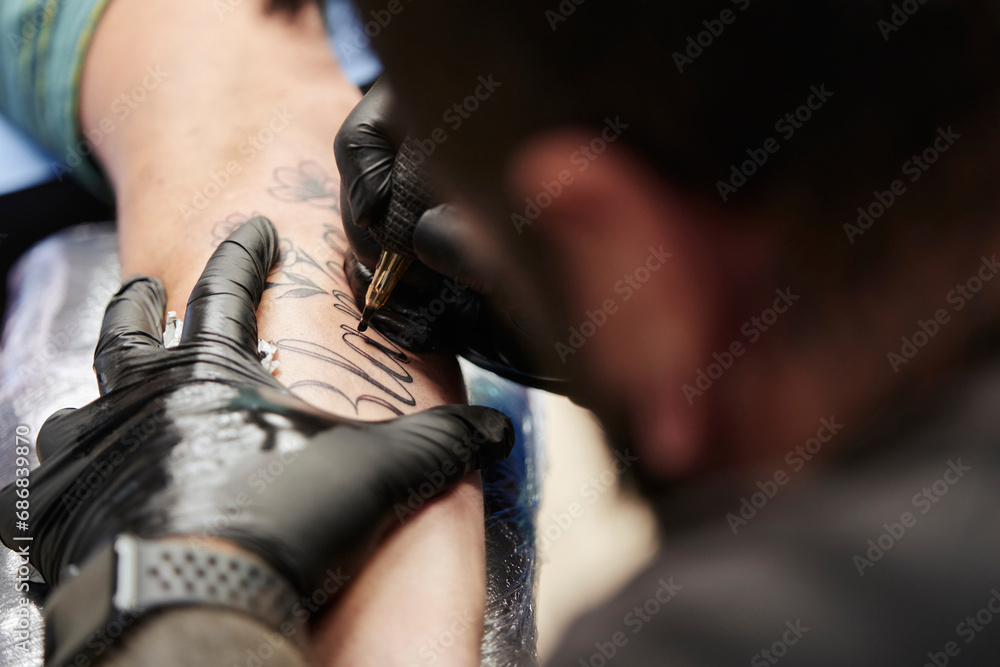 Close-up of male artist tattooing on customer's hand in studio