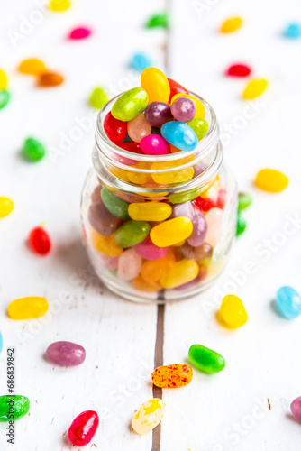 Glass of colourful sweet jellybeans on white wood
